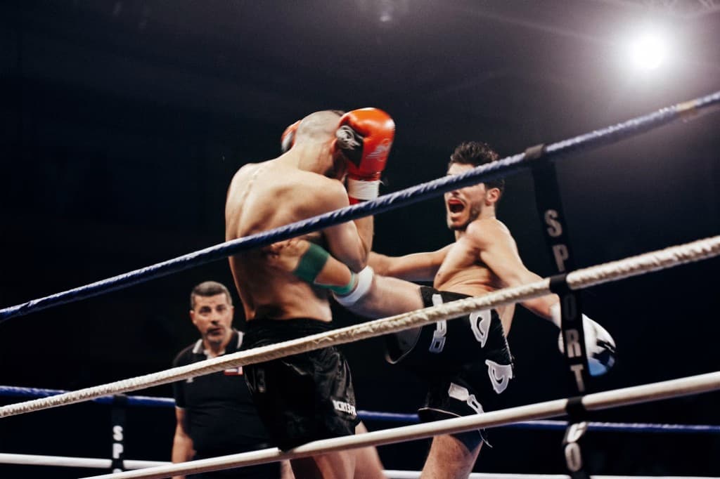 Kickboxer landing a head kick over a high guard, upper body leaning back to stay balanced — the balance Form Fighter tracks through the throw.